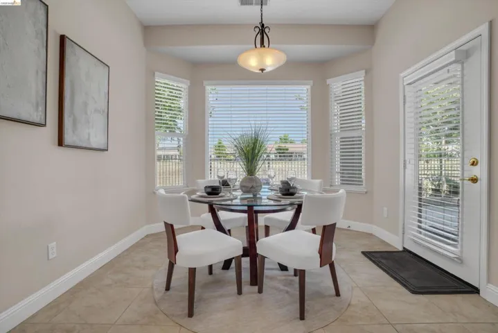 Bay window dining area featuring a pendant light fixture, tile flooring, and a glass-paneled door with integrated blinds