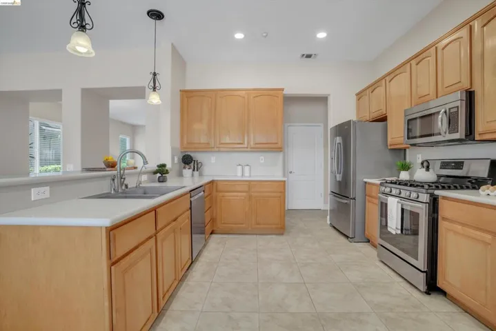Kitchen featuring wood-finish cabinetry, stainless steel appliances, light countertops, and tile flooring