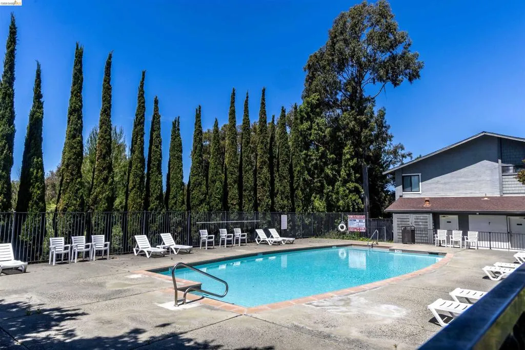 Community swimming pool featuring a dark-colored fence and surrounding concrete decking