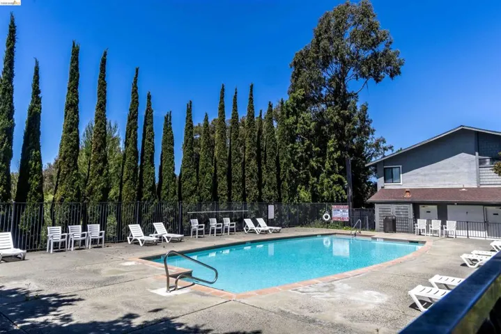 Community swimming pool featuring a dark-colored fence and surrounding concrete decking