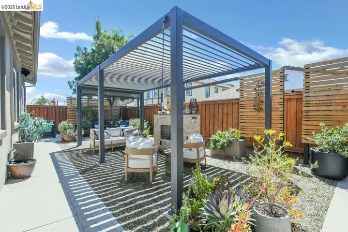 Outdoor living area featuring a modern black pergola, a stone-clad outdoor fireplace, and gravel hardscaping