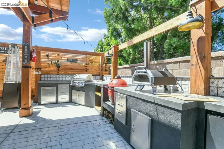 Outdoor kitchen featuring a built-in grill, integrated stainless steel storage, and ample counter space under a wood pergola