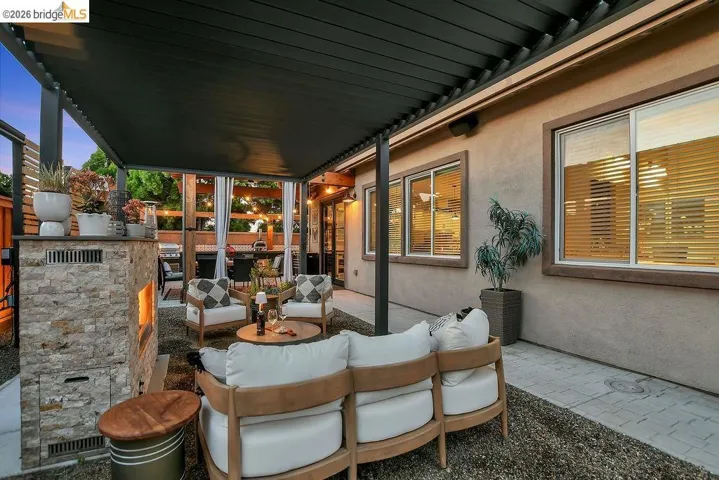 Covered patio featuring a stone-clad outdoor fireplace, aggregate ground cover, and a stucco exterior with multiple window openings