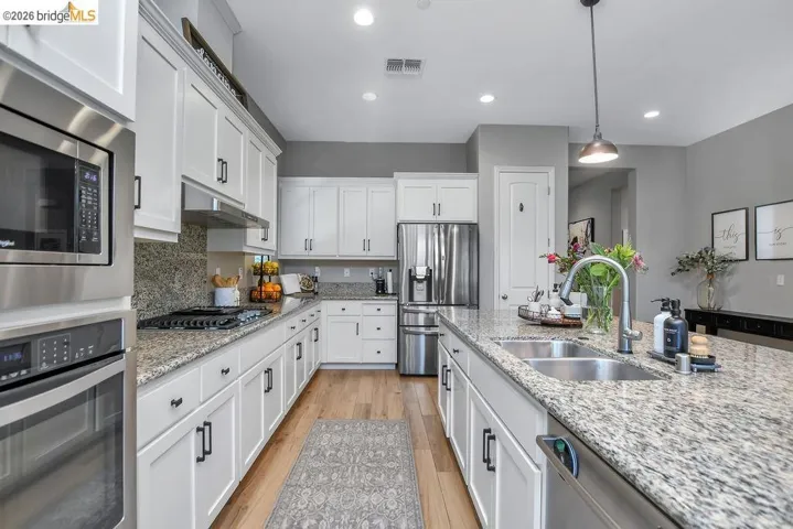 Kitchen featuring light wood-finish flooring, white cabinetry with black hardware, recessed lighting, and granite countertops
