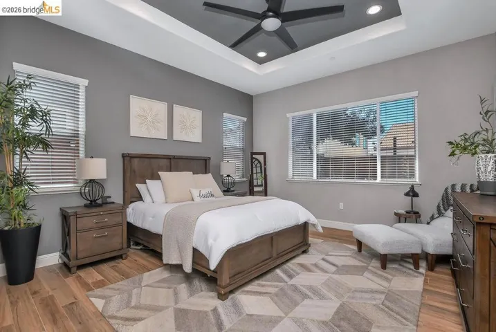 Spacious room featuring wood-finish flooring, a tray ceiling with recessed lighting, and a dark-toned ceiling fan