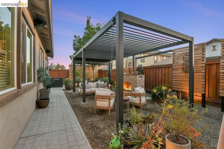 Outdoor living area featuring a modern pergola, a built-in stone fireplace, a gravel ground cover, and structured wood fencing