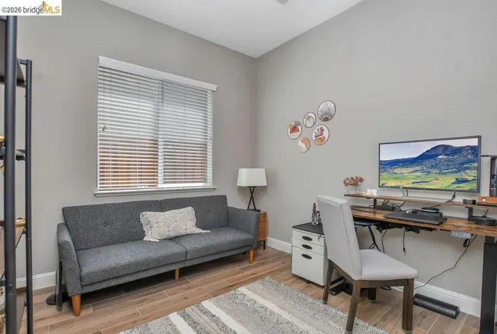 Room featuring wood-finish flooring, a window with horizontal blinds, and a built-in ceiling fan