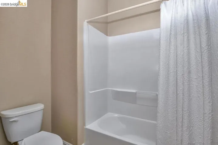 Bathroom featuring a white toilet and a white bathtub with an integrated shower surround