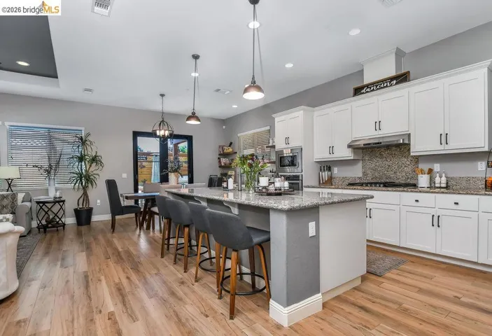 Contemporary kitchen featuring white cabinetry, integrated stainless steel appliances, a multi-tone granite countertop, and a coordinating backsplash