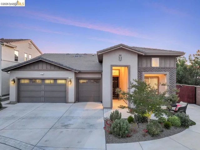 Contemporary stucco exterior with brick accents, an integrated two-car garage, an additional single-car garage, a tiled roof, and established landscaping