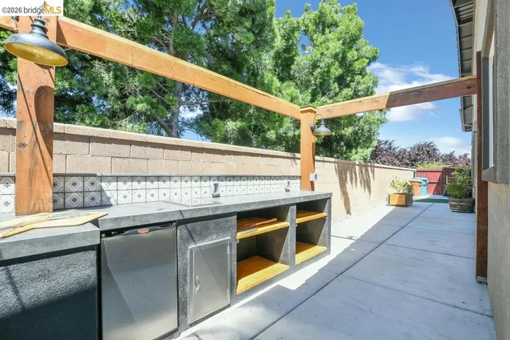 Outdoor kitchen featuring a built-in refrigerator, under-counter shelving, and a patterned tile backsplash
