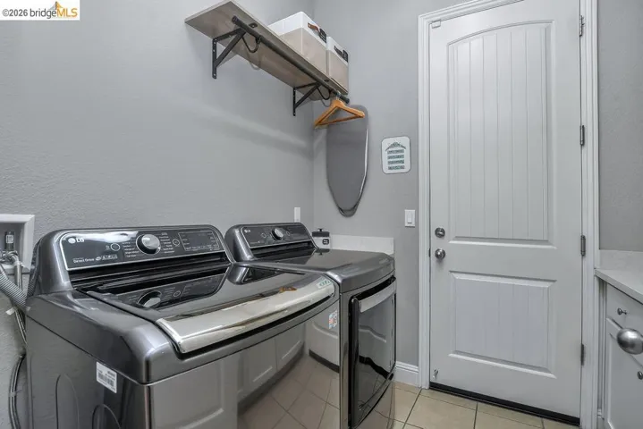 Dedicated laundry room featuring light gray walls, tile flooring, a built-in shelving unit, and a white paneled door