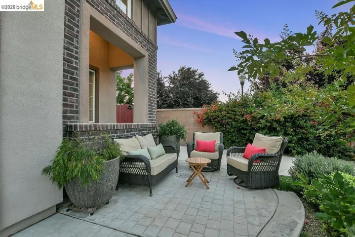 Covered patio featuring a patterned paver surface, stucco and brick exterior accents, and perimeter landscaping