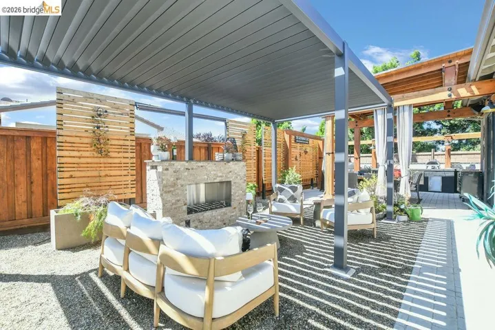 Outdoor living space featuring a louvered pergola, stone-clad fireplace, and mixed paver and gravel flooring
