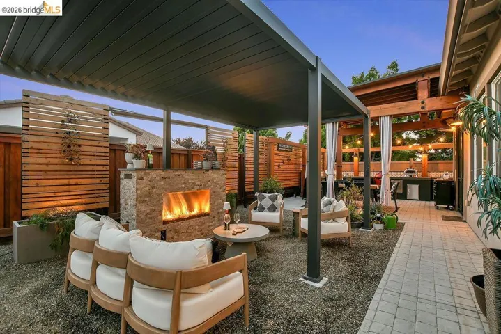 Outdoor living area featuring a louvered pergola, stone-clad fireplace, gravel ground cover, and wood privacy screens