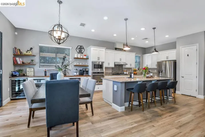 Open-concept kitchen and dining area featuring light wood-finish flooring, white cabinetry, and stainless steel appliances