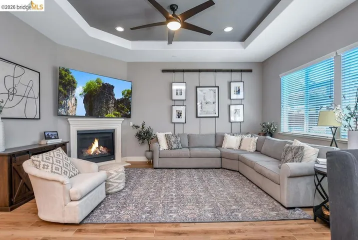 Spacious living room featuring wood-finish flooring and a tray ceiling with a ceiling fan