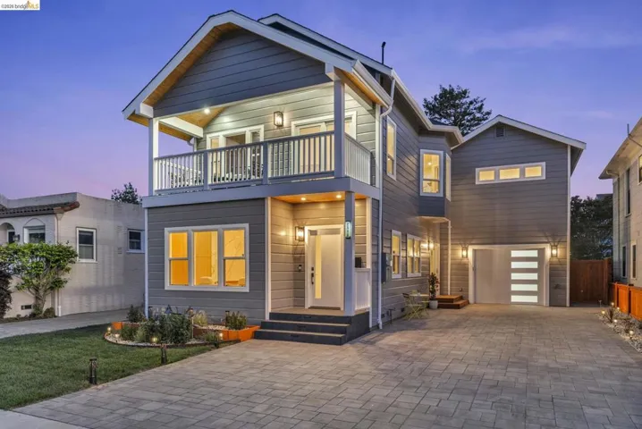 Contemporary two-story exterior featuring a second-level balcony, a modern garage door with frosted glass panels, a paver driveway, and exterior lighting fixtures