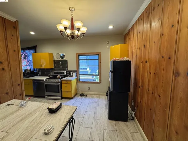 Kitchen featuring wood-paneled walls, a five-light chandelier, a stainless steel range, and light-colored tile flooring