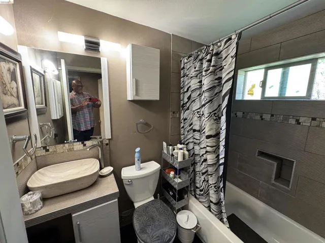 Bathroom featuring a vessel sink, vanity with under-sink storage, wall-mounted mirror, and a bathtub with tiled surround