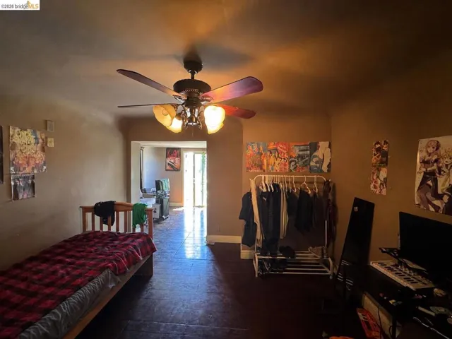 Room featuring a ceiling fan with integrated lighting, wood-finish flooring, and a doorway opening to another area with natural light