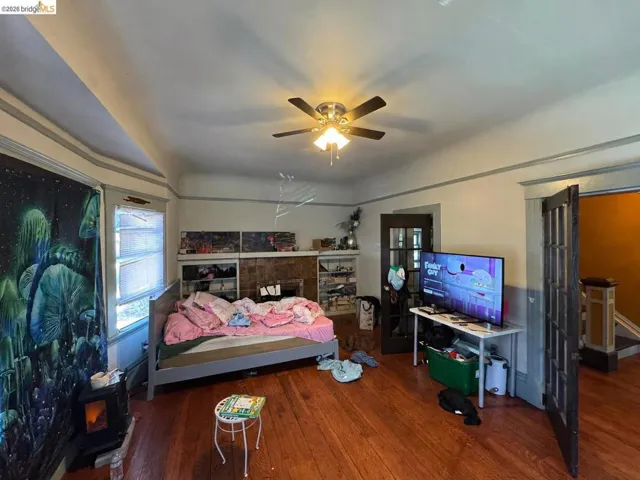 Spacious room featuring wood-finish flooring, a ceiling fan with integrated lighting, and a fireplace with a tile surround and built-in shelving