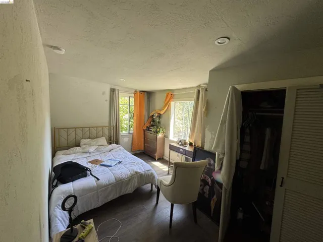 Bedroom featuring dark wood-finish flooring and two windows with natural light