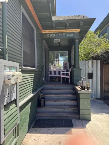 Covered front porch with decorative trim, exterior wall sconce, and a prominent house number display