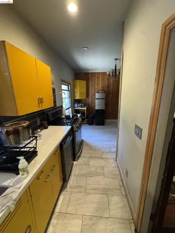 Galley kitchen featuring light-toned tiled flooring, white countertops, and yellow cabinetry