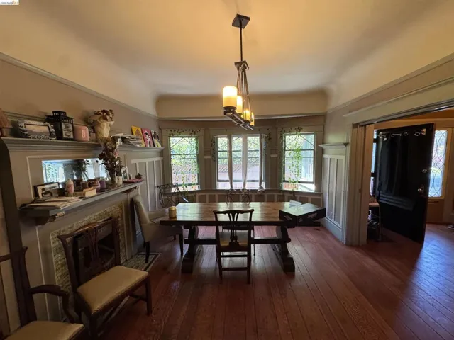Dining area featuring rich wood-finish flooring, a decorative fireplace with a mantel, multiple casement windows, wainscoting, and a multi-light chandelier