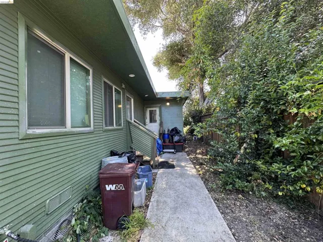 Exterior walkway leading to an entry door, bordered by mature trees and lush plantings