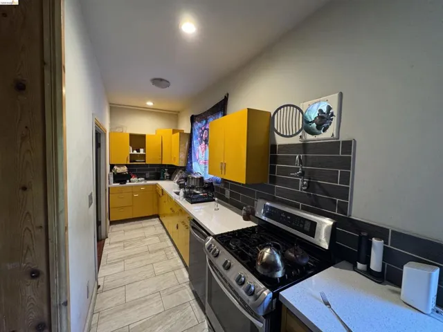 Kitchen featuring vibrant yellow cabinetry, white countertops, and a dark tile backsplash