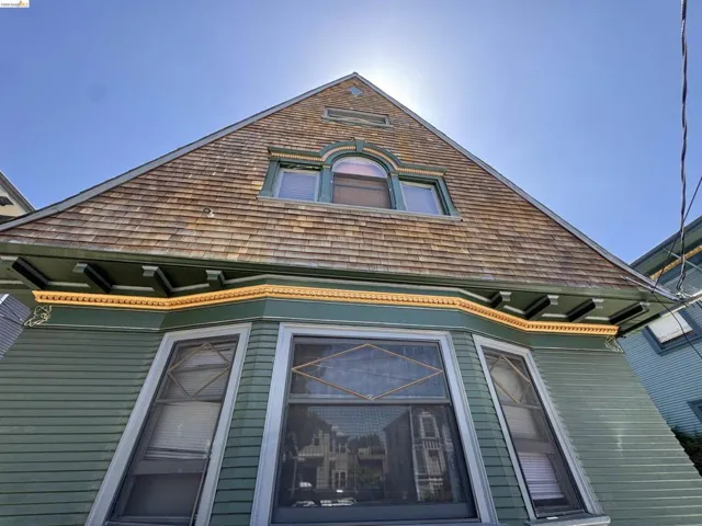 Gable-front facade featuring cedar shake siding, decorative trim, a bay window with diamond-patterned mullions, and an arched dormer window