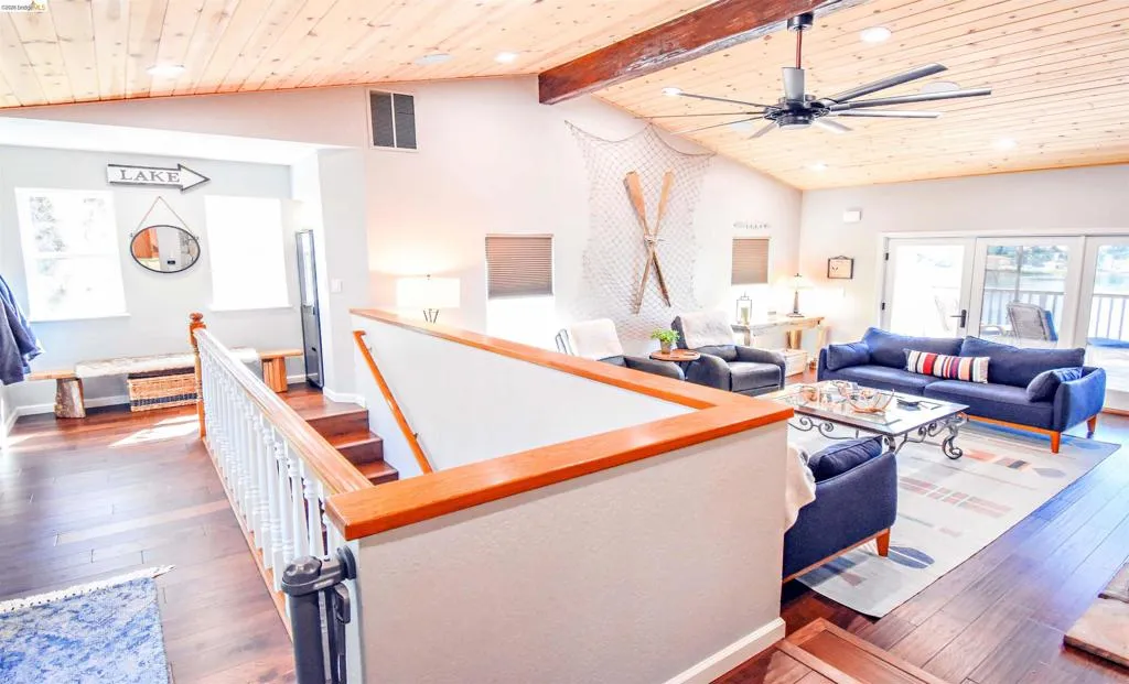 Spacious living area featuring a vaulted wood-paneled ceiling, exposed wood beams, a large ceiling fan, dark wood-finish flooring, and glass doors leading to an exterior space