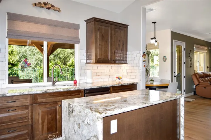 This Recently Remodeled Kitchen Boasts Gorgeous Slab Granite Countertops with Waterfall Edges on the Island, Soft-Close KraftMaid Cabinetry with Customized Inserts, Stainless Steel Appliances (Slide-in Gas Range with Dual Convection Ovens, Attractive Hood, and Super-Quiet Dishwasher), Stylish Tile Backsplash, Beautiful Shades, and a Dual Basin Porcelain Sink with Tree-Filled Backyard Views Atop Engineered Hardwood Flooring