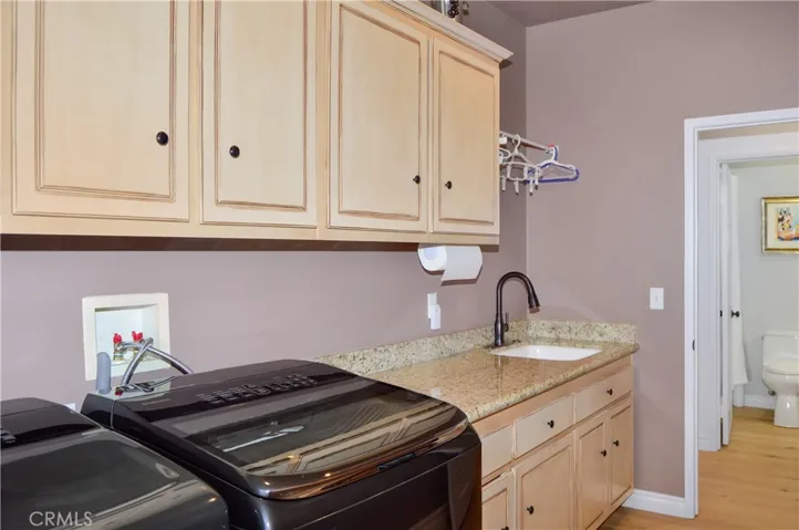 The Laundry/Utility Room is on the Main Floor and Features a Porcelain Sink, Granite Countertop, Abundant Cabinetry, Engineered Hardwood Flooring, and a Door to the Backyard.