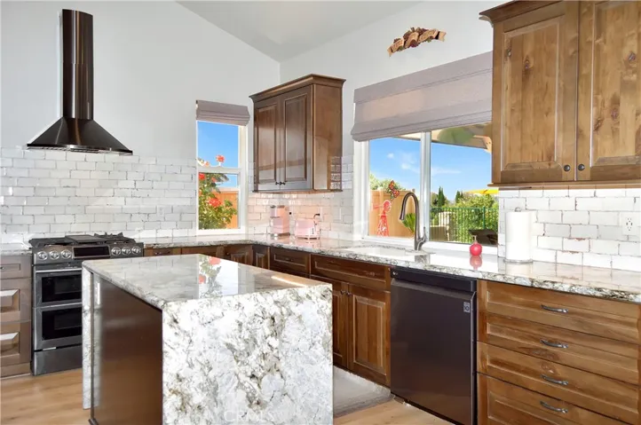 Gorgeous Slab Granite Countertops with Waterfall Edges, Soft-Close KraftMaid Cabinetry with Customized Inserts, Stainless Steel Appliances (Slide-in Gas Range with Dual Convection Ovens, Attractive Hood, and Super-Quiet Dishwasher), Stylish Tile Backsplash, Beautiful Shades, and a Dual Basin Porcelain Sink with Tree-Filled Backyard Views Atop Engineered Hardwood Flooring