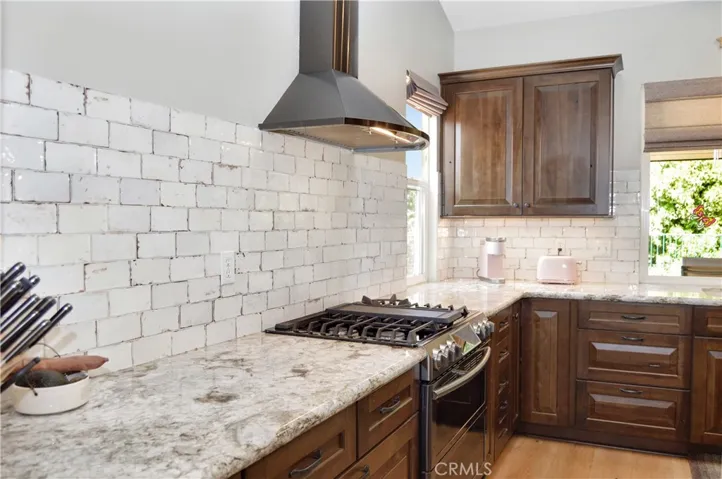 This Recently Remodeled Kitchen Boasts Gorgeous Slab Granite Countertops with Waterfall Edges on the Island, Soft-Close KraftMaid Cabinetry with Customized Inserts, Stainless Steel Appliances (Slide-in Gas Range with Dual Convection Ovens, Attractive Hood, and Super-Quiet Dishwasher), Stylish Tile Backsplash, Beautiful Shades, and a Dual Basin Porcelain Sink with Tree-Filled Backyard Views Atop Engineered Hardwood Flooring