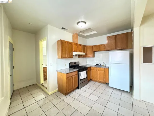 Kitchen featuring brown cabinets, stainless steel gas range, freestanding refrigerator, light tile patterned floors, and decorative backsplash