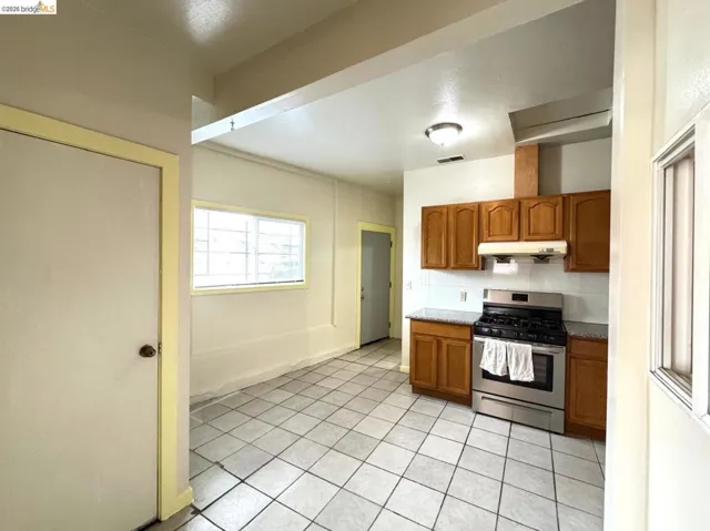 Kitchen featuring brown cabinetry, gas stove, under cabinet range hood, light tile patterned floors, and tasteful backsplash