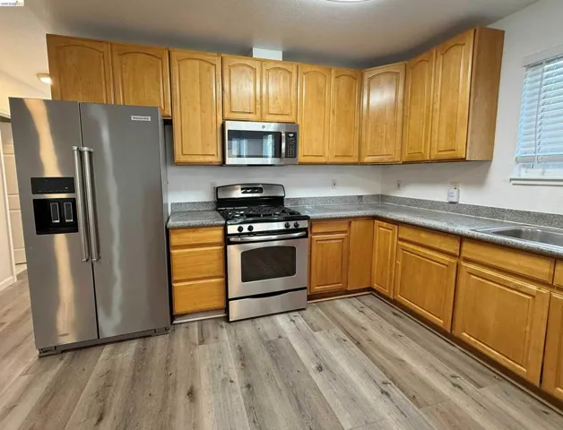 Kitchen featuring wood-finish cabinetry, stainless steel appliances, speckled countertops, and wood-finish flooring