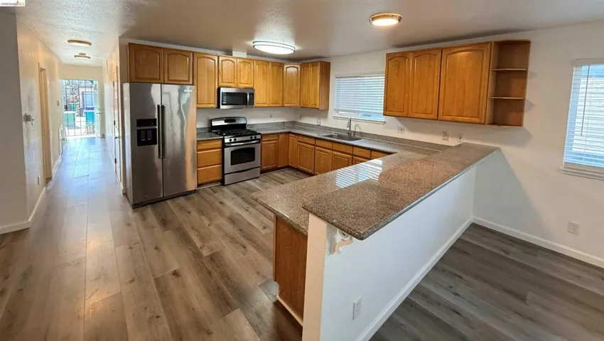 Kitchen featuring wood-finish cabinetry, stainless steel appliances, granite-style countertops, and wood-finish flooring