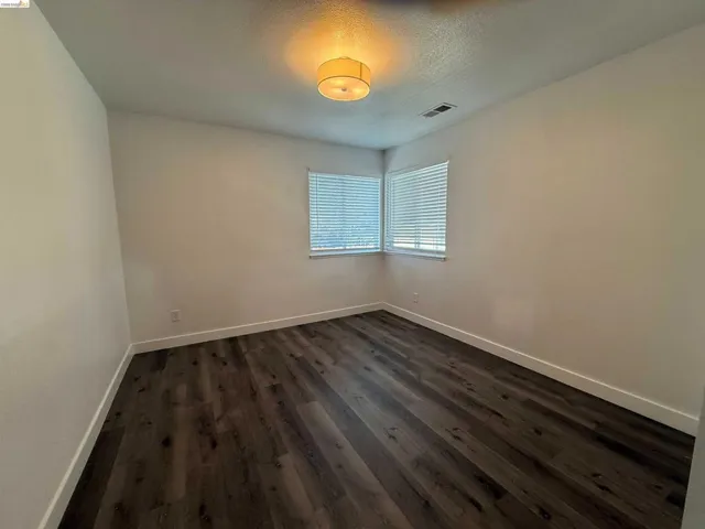 Spacious room featuring wood-finish flooring, two windows with blinds, a ceiling-mounted light fixture, and white baseboards