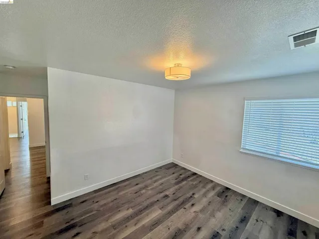 Spacious room featuring wood-finish flooring, white walls, and a contemporary flush-mount ceiling light