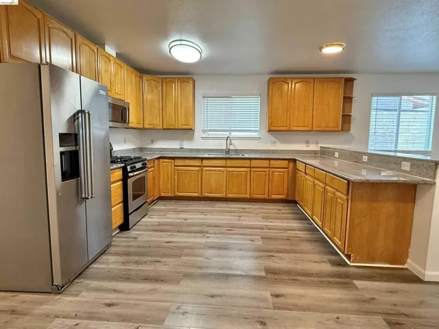 Spacious kitchen featuring extensive cabinetry, stone countertops, stainless steel appliances, wood-finish flooring, and recessed lighting