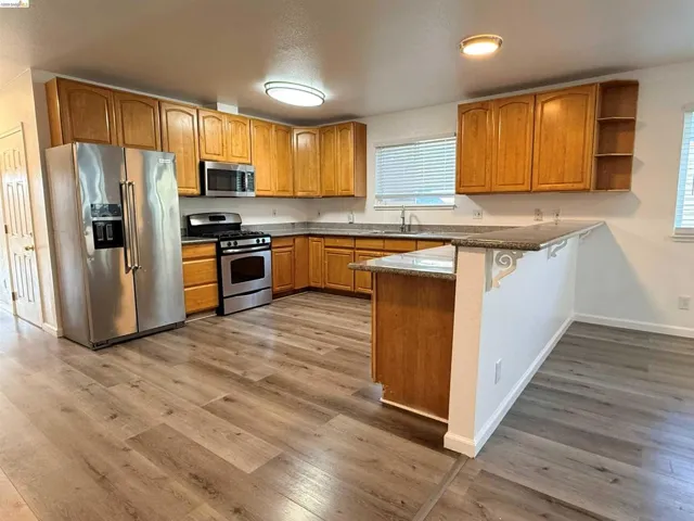 Kitchen featuring wood-finish flooring, L-shaped cabinetry, stainless steel appliances, a built-in microwave, and a breakfast bar with decorative corbels