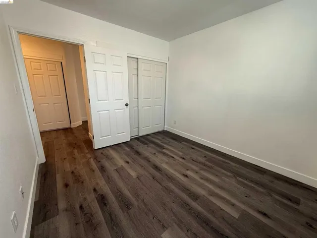Spacious room featuring wood-finish flooring, white walls, and a multi-panel door