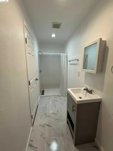 Bathroom featuring a standing shower with white tile surround, a single vanity with a gray cabinet base and integrated sink, a mirrored medicine cabinet, and marble-look floor tiles
