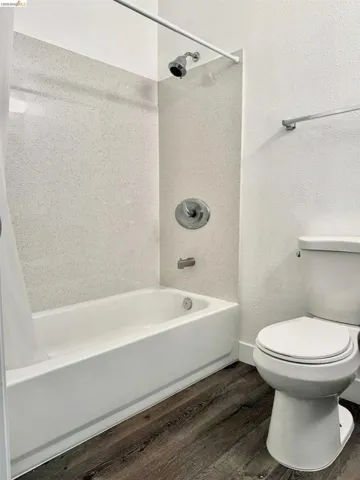 Bathroom featuring a white bathtub with speckled wall surround, chrome fixtures, and wood-finish flooring