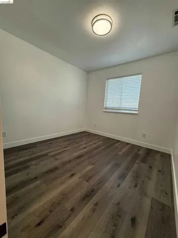 Room featuring wood-finish flooring, white baseboards, a single window with horizontal blinds, and a ceiling-mounted flush light fixture
